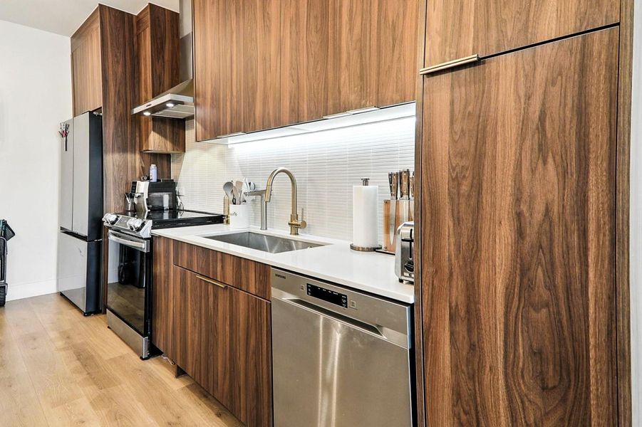 Kitchen with stainless steel appliances, modern cabinets, light wood-style flooring, and light countertops