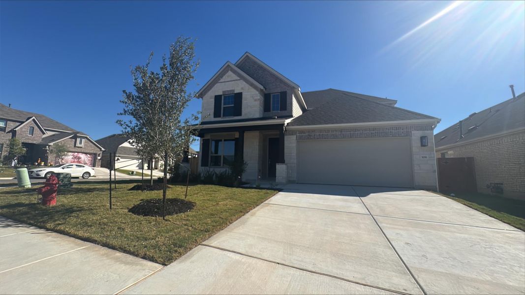 Traditional-style house featuring stone siding, a front lawn, driveway, a garage, and covered porch