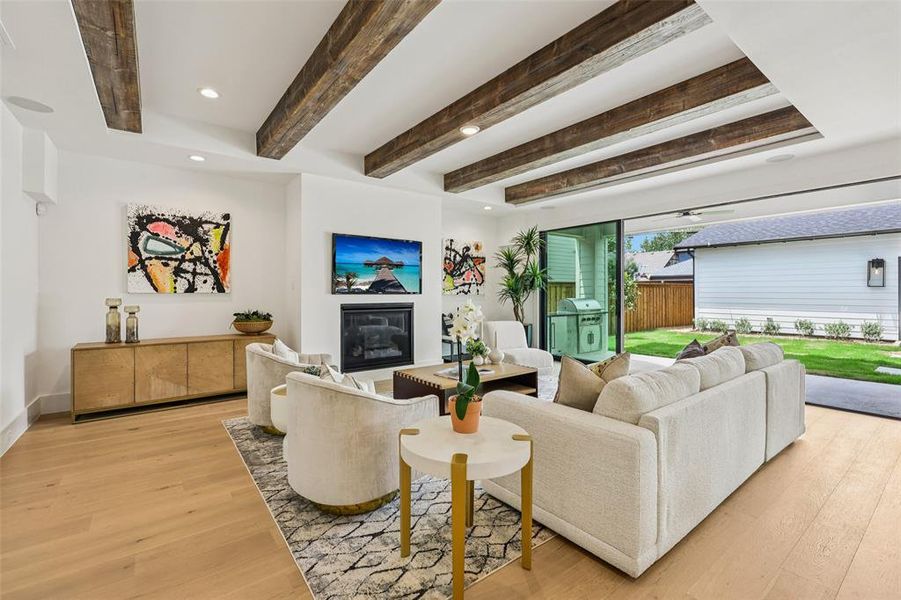 Spacious living area featuring exposed wood ceiling beams, light wood-finish flooring, and a built-in fireplace