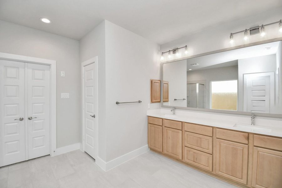 Escape to a spa-like oasis in this primary bathroom. Enjoy a walk-in shower with tile surround, a separate garden tub with custom detailing, and an elegant vanity featuring light countertops, modern hardware, and beautiful vanity lights. Experience luxury and relaxation in every detail. Sample photo of completed home with similar floor plan. Actual colors and selections may vary.