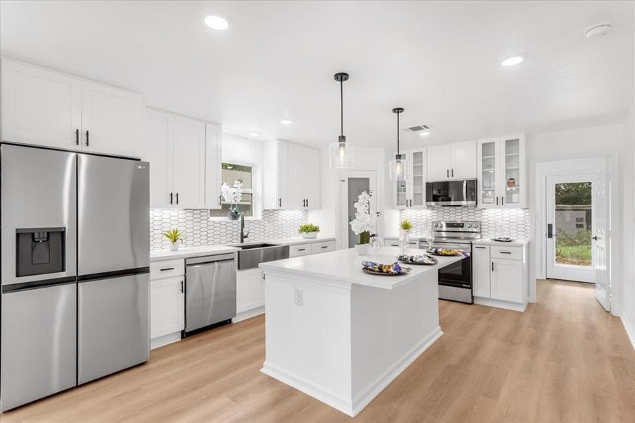 Kitchen with deep farmhouse sink, a center island, light wood floors, stainless steel appliances, and white cabinets