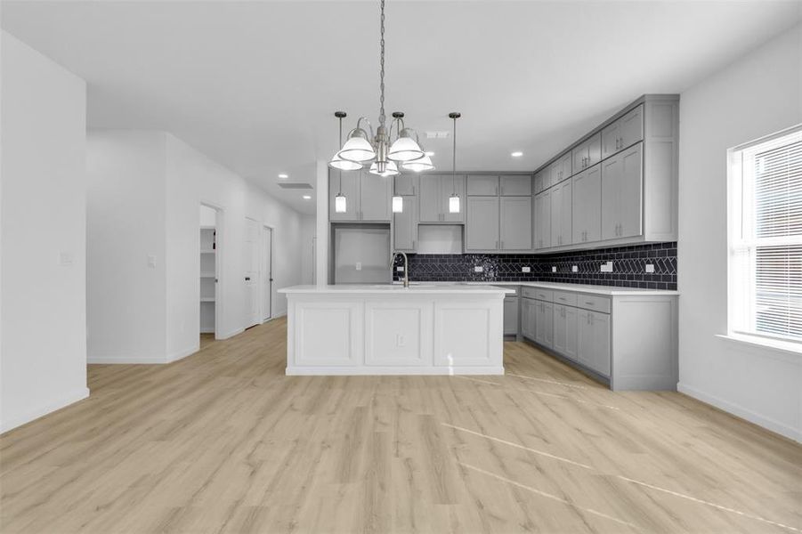 Kitchen featuring gray cabinetry, light wood-style floors, a center island with sink, pendant lighting, and open floor plan