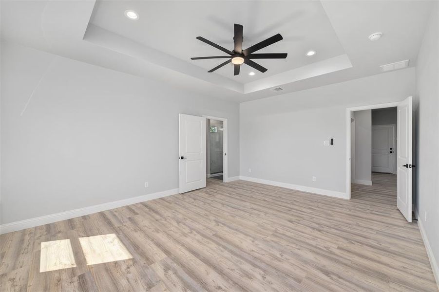 Unfurnished bedroom with light wood-style flooring, visible vents, and a raised ceiling