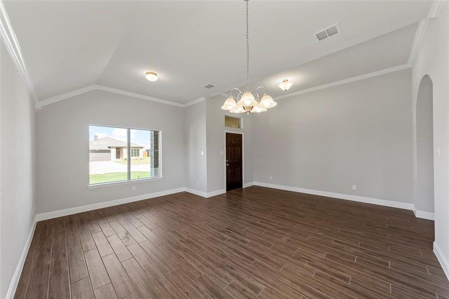 Empty room with a chandelier, dark wood-type flooring, lofted ceiling, and ornamental molding