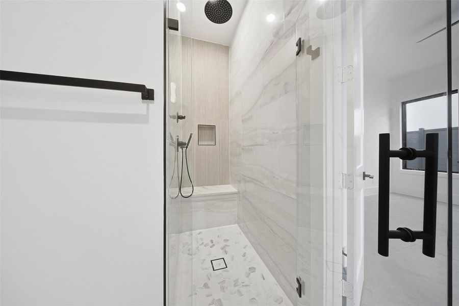 The walk-in shower includes a black rain showerhead, a built-in marble bench, and a recessed niche for storage.