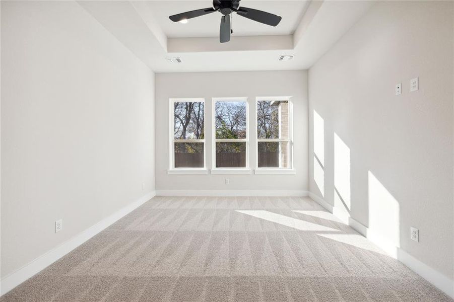 Carpeted empty room featuring a raised ceiling and ceiling fan