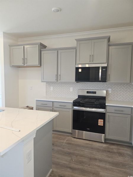 Kitchen with gray cabinets, stainless steel appliances, ornamental molding, decorative backsplash, and light stone counters