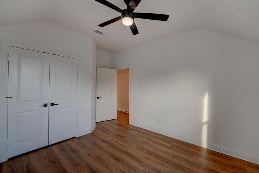 Bedroom with a closet, visible vents, vaulted ceiling, vinyl 
 finished floors, and baseboards