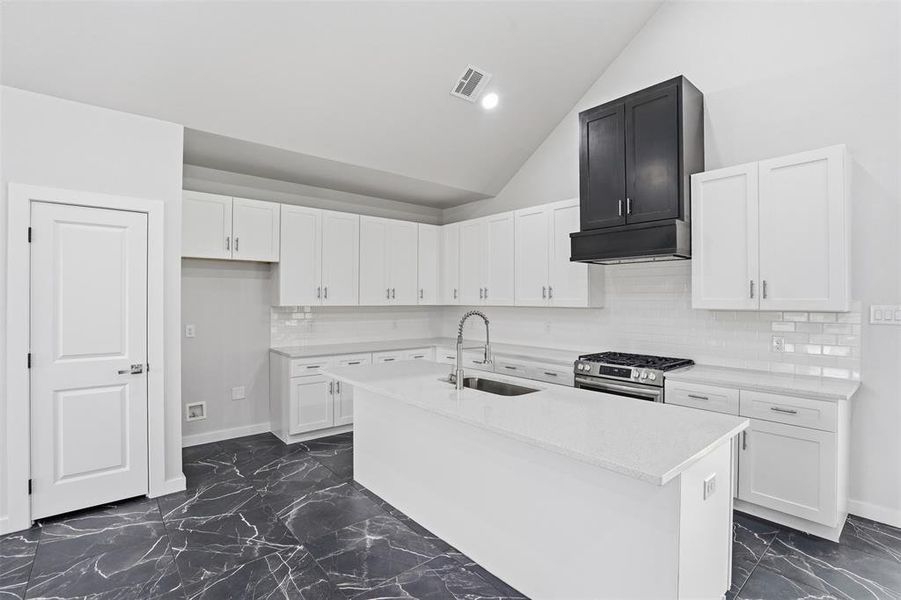 Bright kitchen featuring a central island, white shaker cabinetry, white subway tile backsplash, stainless steel gas range, and a black range hood