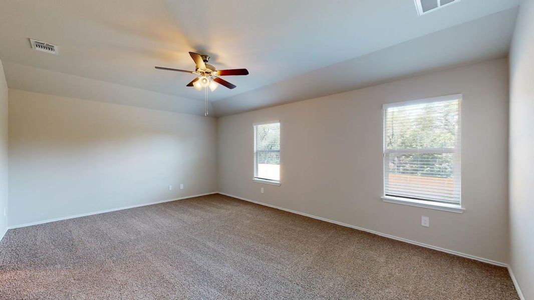 A spacious, naturally illuminated room featuring warm carpeting and a modern ceiling fan for ultimate comfort.
