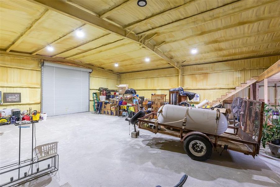 Large interior space featuring a roll-up garage door, concrete flooring, exposed wood beams, and a wood-finish staircase Large interior space featuring a roll-up garage door, concrete flooring, exposed wood beams, and a wood-finish staircase