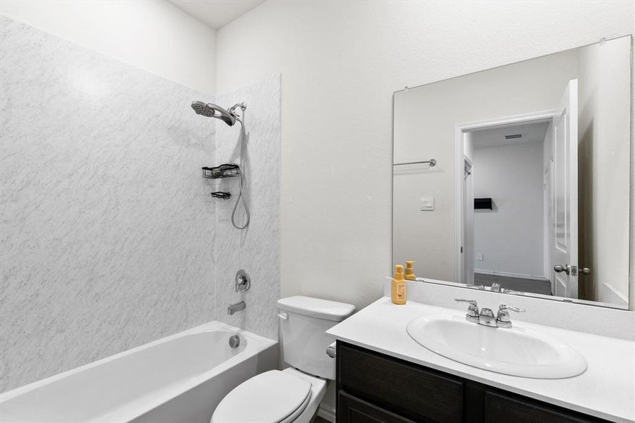 Bathroom featuring a white bathtub, a toilet, a dark wood-finish vanity with a white countertop, and an oval undermount sink