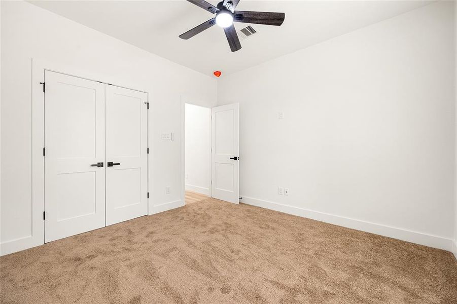 This room features a neutral-toned carpet, white walls, a ceiling fan, and double closet doors. It offers a clean, bright space with modern finishes and an open entryway to adjacent rooms.