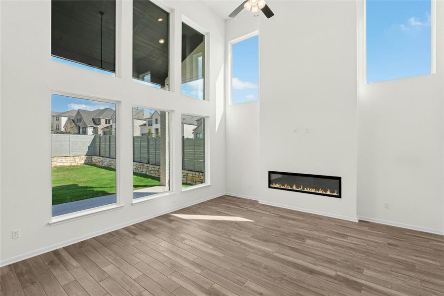 Unfurnished living room featuring plenty of natural light, a high ceiling, a glass covered fireplace, a ceiling fan, and wood finished floors Unfurnished living room featuring plenty of natural light, a high ceiling, a glass covered fireplace, a ceiling fan, and wood finished floors