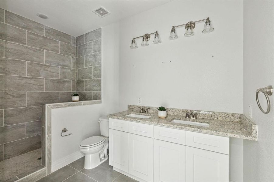 Bathroom with vanity, toilet, tiled shower, and tile patterned floors