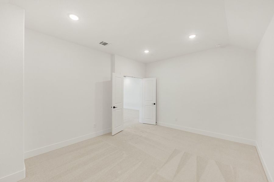 Empty bedroom with white walls, beige carpet, recessed lighting, and open closet doors