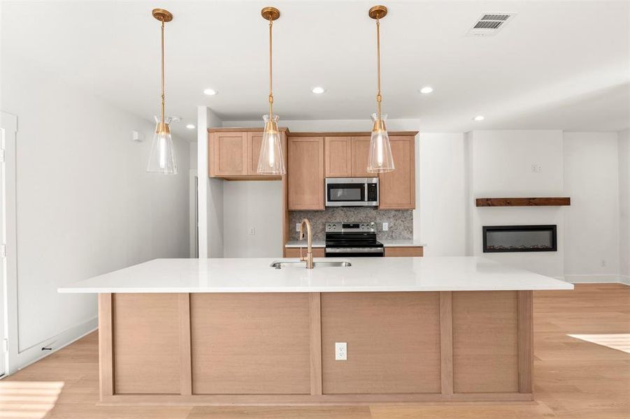Kitchen with backsplash, stainless steel appliances, light wood-type flooring, pendant lighting, and light stone counters