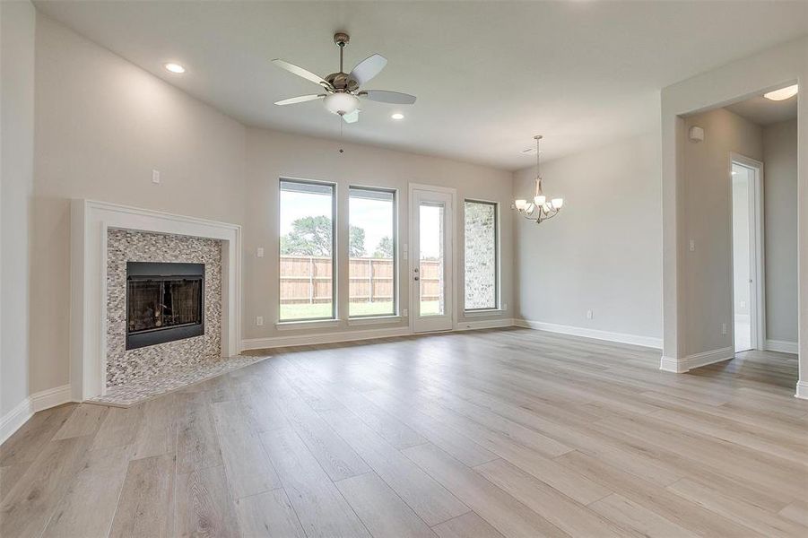 Unfurnished living room with a tile fireplace, light wood-type flooring, and ceiling fan with notable chandelier