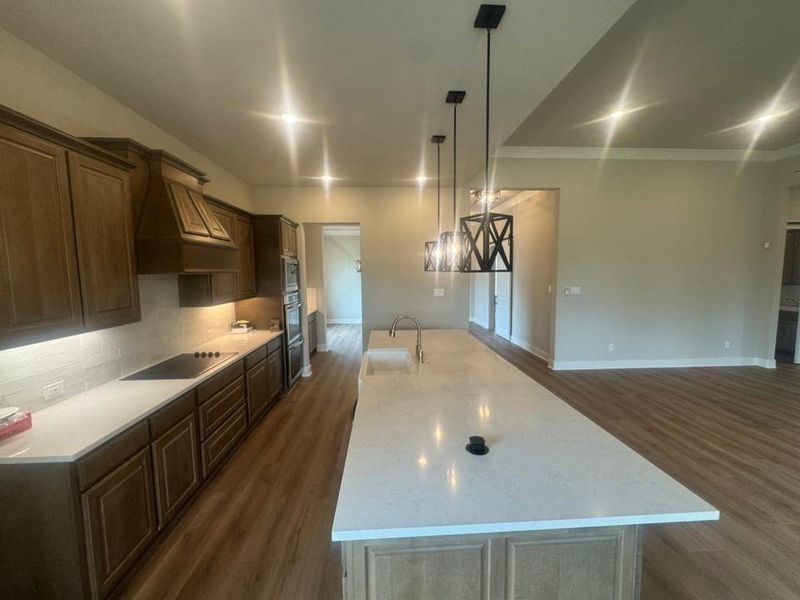 Kitchen featuring a spacious island with an undermount sink and gold-tone faucet, dark wood cabinetry, white countertops, and a subway tile backsplash