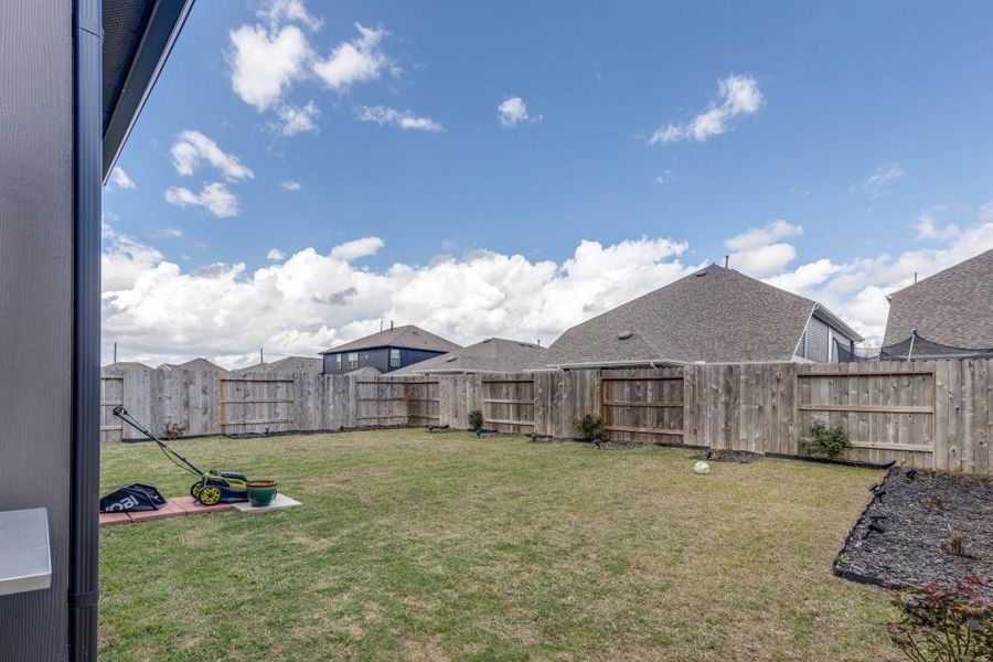 Spacious backyard with a well-maintained lawn, enclosed by a wooden fence. Ideal for outdoor activities and gardening, with a clear view of the neighboring rooftops under a partly cloudy sky.