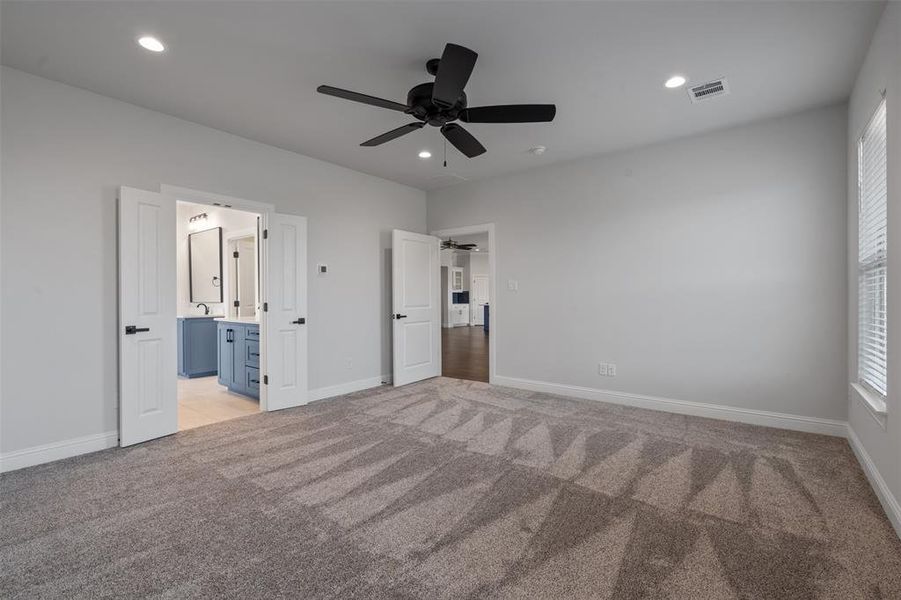 Unfurnished bedroom with ceiling fan, multiple windows, connected bathroom, and light carpet