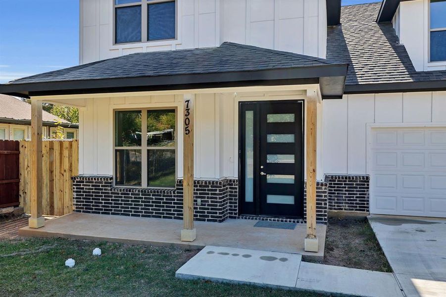 Property entrance featuring board and batten siding, roof with shingles, and brick siding