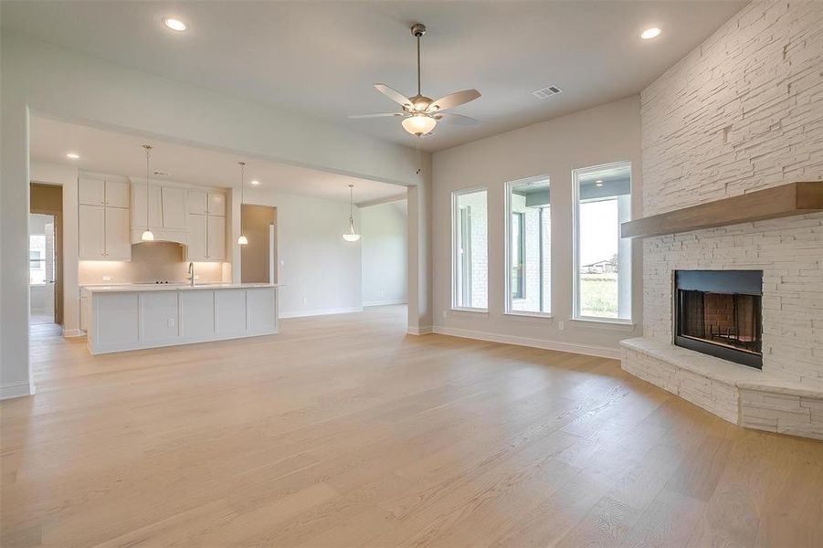 Unfurnished living room with ceiling fan, light wood-type flooring, sink, and a stone fireplace