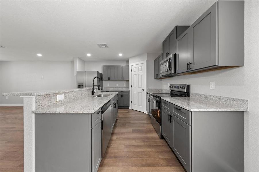 Kitchen featuring appliances with stainless steel finishes, gray cabinets, dark wood finished floors, light stone counters, and recessed lighting Kitchen featuring appliances with stainless steel finishes, gray cabinets, dark wood finished floors, light stone counters, and recessed lighting