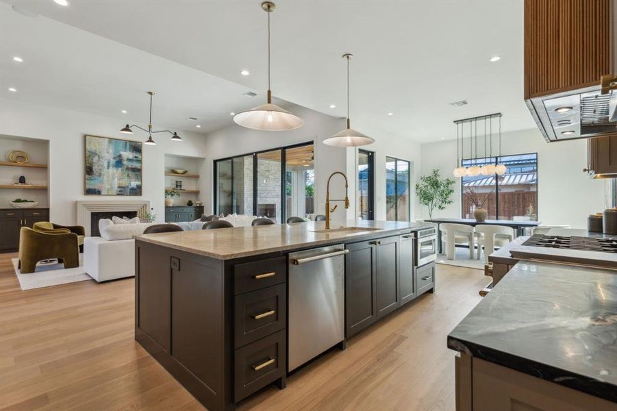 Kitchen with dishwasher, sink, built in shelves, dark stone countertops, and a large island