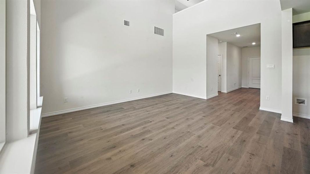Spacious room featuring wood-finish flooring, high ceilings, multiple windows, and a wide entryway Spacious room featuring wood-finish flooring, high ceilings, multiple windows, and a wide entryway
