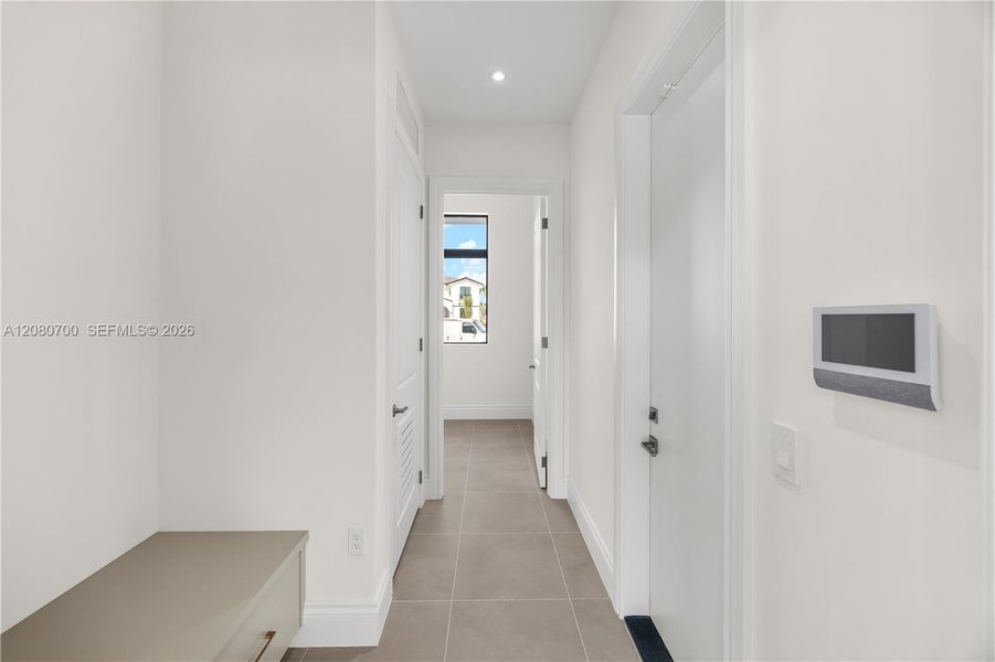 Recessed lighting illuminates a hallway with neutral-toned floor tiling