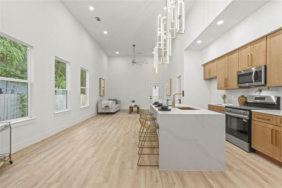 Kitchen featuring stainless steel appliances, a sink, a high ceiling, recessed lighting, and light wood finished floors Kitchen featuring stainless steel appliances, a sink, a high ceiling, recessed lighting, and light wood finished floors
