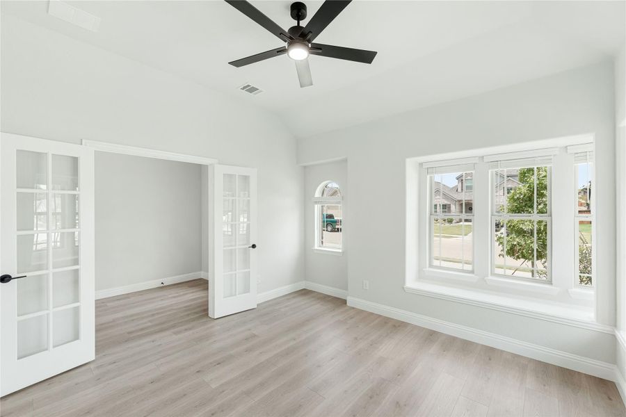 Empty room with light wood floors, ceiling fan, French doors, and large windows with neighborhood view