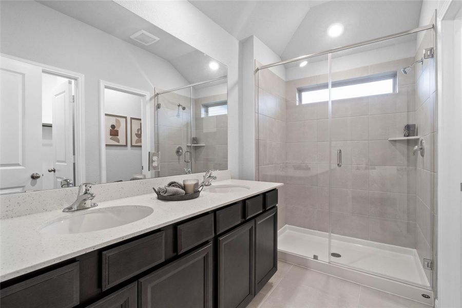 Relax and unwind in this contemporary en-suite bathroom, featuring a dual vanity with sleek dark cabinetry and quartz countertops, a spacious walk-in shower with stylish tile surround, and abundant natural light.