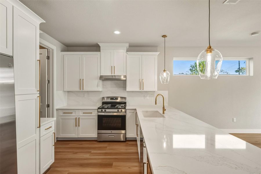 Modern kitchen with white cabinetry and sleek hardware, featuring a spacious marble countertop and stainless steel appliances. Pendant lighting and a large window provide ample natural light. Modern kitchen with white cabinetry and sleek hardware, featuring a spacious marble countertop and stainless steel appliances. Pendant lighting and a large window provide ample natural light.