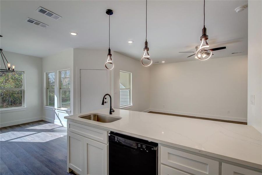 Kitchen featuring black dishwasher, dark wood-style floors, decorative light fixtures, light stone countertops, and white cabinets Kitchen featuring black dishwasher, dark wood-style floors, decorative light fixtures, light stone countertops, and white cabinets