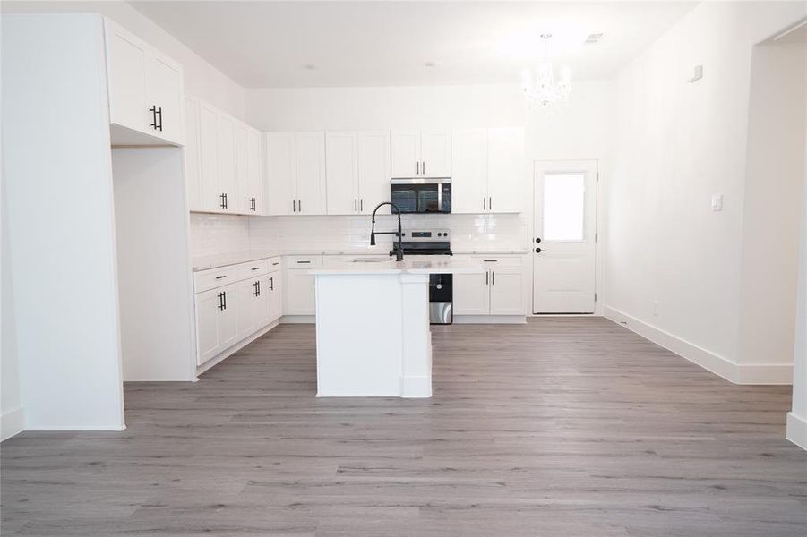 Kitchen featuring backsplash, white cabinets, appliances with stainless steel finishes, and light wood-style floors