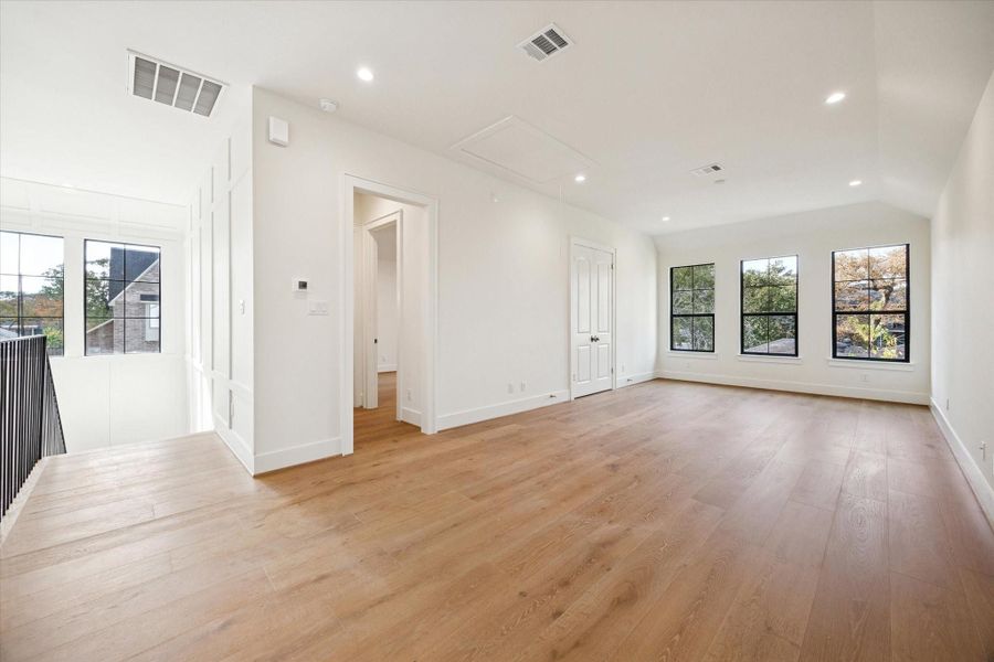 Upstairs game room with white oak wood flooring, recessed lighting, and large windows.