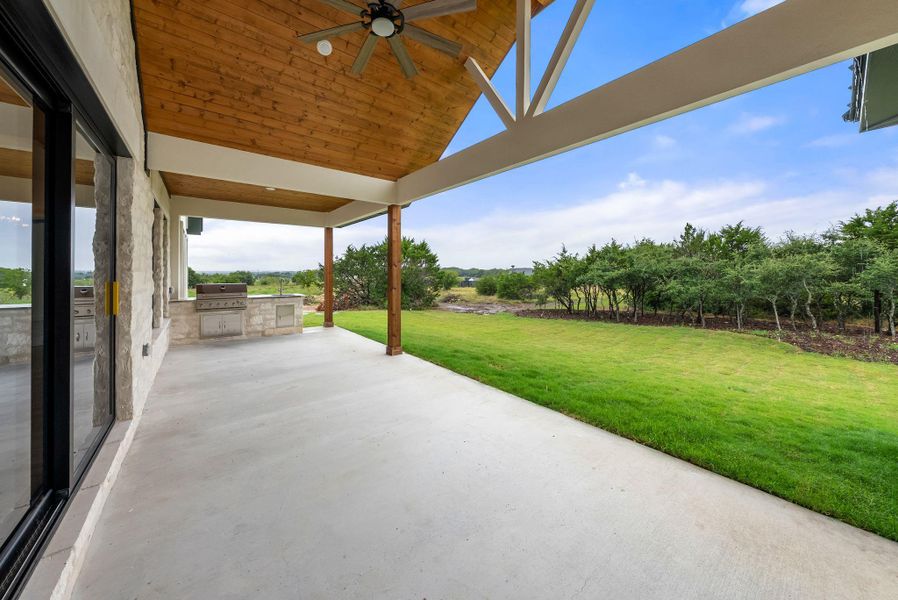 An inviting covered patio offers ample space for entertaining with an outdoor kitchen, leading to a vibrant green lawn.