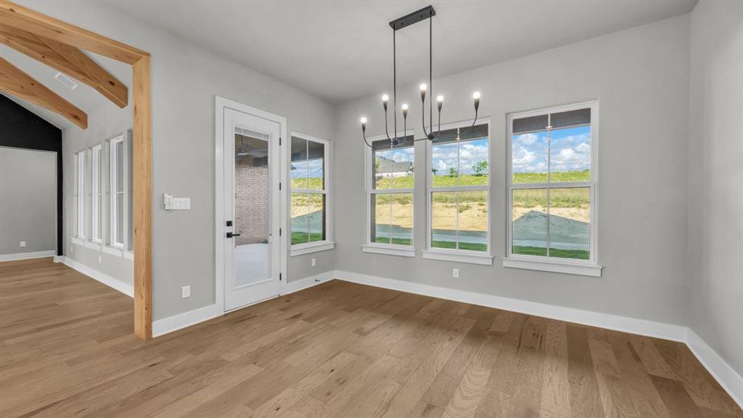 Open-concept interior featuring wood-finish flooring, a contemporary chandelier, multiple windows with white trim, and a glass-paned door Open-concept interior featuring wood-finish flooring, a contemporary chandelier, multiple windows with white trim, and a glass-paned door