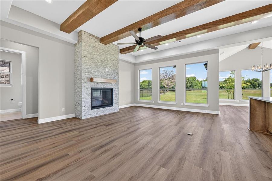 Spacious living area featuring wood-finish flooring, a stacked stone fireplace with a wood mantle, and exposed wood ceiling beams
