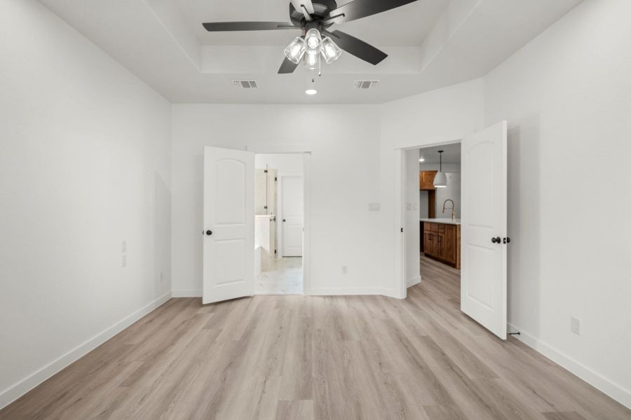 A spacious primary bedroom features tray ceilings and light-hued hardwood flooring throughout. A spacious primary bedroom features tray ceilings and light-hued hardwood flooring throughout.