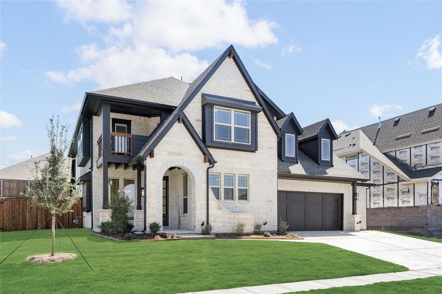 Two-story home with cream stone exterior, dark trim, arched entry, and two-car garage with green front lawn Two-story home with cream stone exterior, dark trim, arched entry, and two-car garage with green front lawn