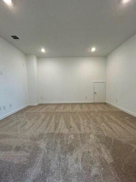Spacious room featuring new carpeting, recessed lighting, white walls, white baseboards, and a white interior door
