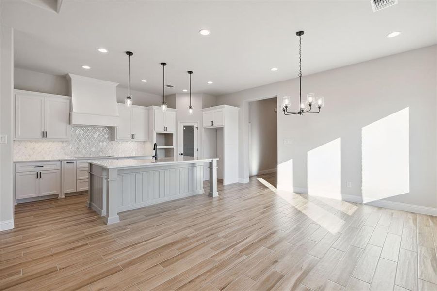 Kitchen with custom exhaust hood, an inviting chandelier, white cabinets, hanging light fixtures, and an island with sink