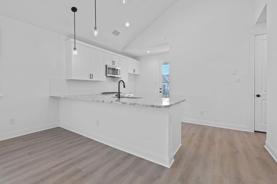 Kitchen featuring light stone countertops, white cabinetry, decorative backsplash, high vaulted ceiling, and light wood-style flooring Kitchen featuring light stone countertops, white cabinetry, decorative backsplash, high vaulted ceiling, and light wood-style flooring
