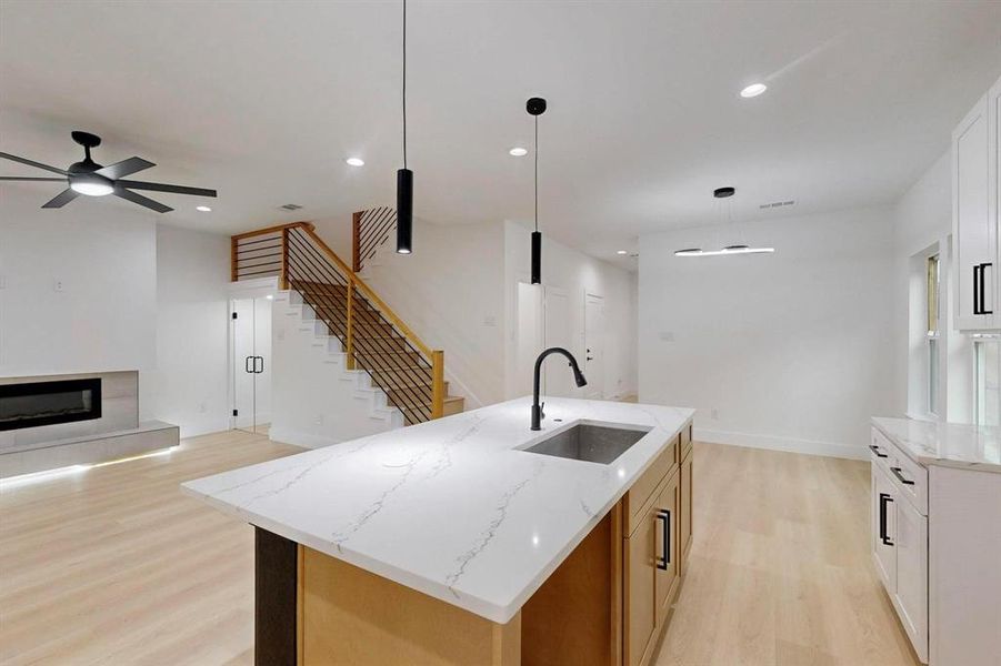 Kitchen featuring a glass covered fireplace, light wood-style floors, a kitchen island with sink, open floor plan, and light stone countertops Kitchen featuring a glass covered fireplace, light wood-style floors, a kitchen island with sink, open floor plan, and light stone countertops