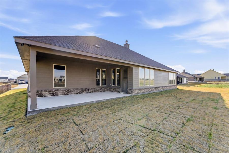 Rear view of property featuring a yard, a patio area, a chimney, roof with shingles, and stone siding