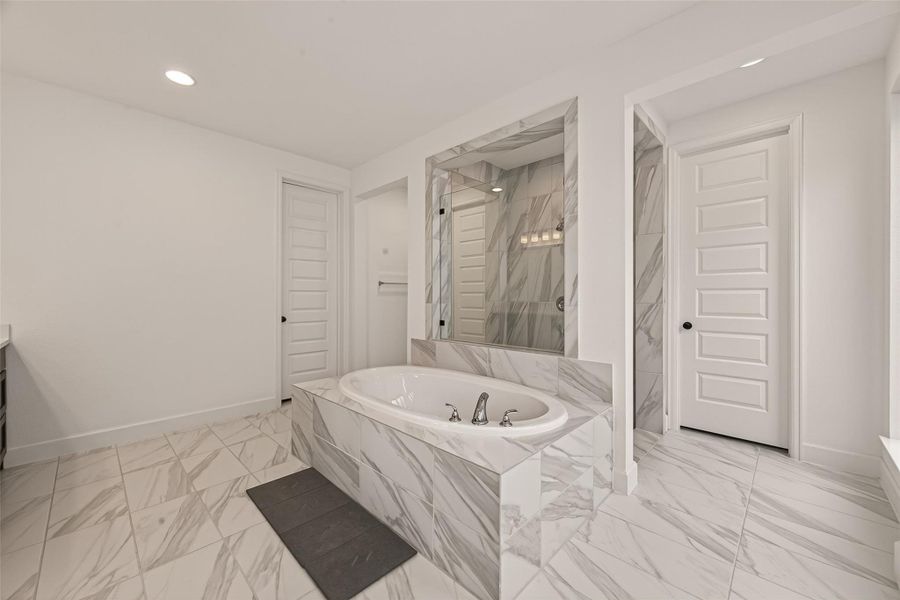 This spacious bathroom features elegant marble tile flooring and walls, a luxurious soaking tub, and a separate shower. The design is modern and bright, with clean lines and ample lighting.