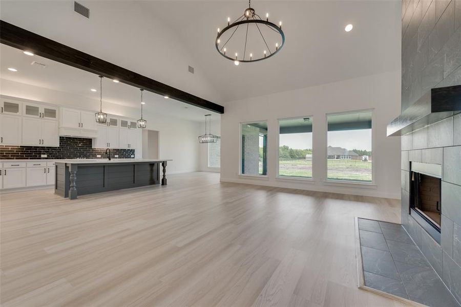 Unfurnished living room featuring beam ceiling, a notable chandelier, light hardwood / wood-style floors, a tiled fireplace, and high vaulted ceiling